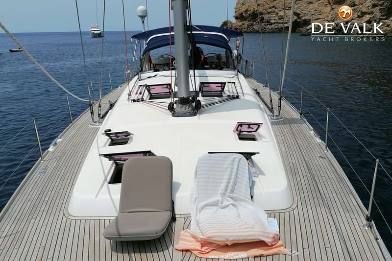 Een zeilboot met een teakhouten dek en een witte opbouw ligt voor anker in een baai. — Beneteau Oceanis 58