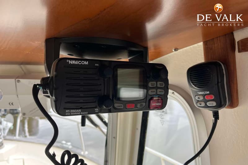 Een Navicom RT-550AIS DSC marifoon met een losse microfoon hangt onder een houten paneel.