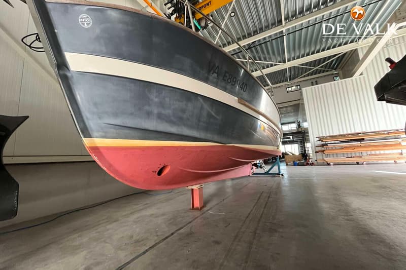 Een donkergrijze boot met een rode onderkant en een crèmekleurige streep, staand op bokken in een loods. — Rhea Marine 750