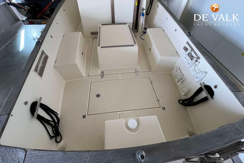De foto toont het interieur van een boot met beige dek en zitplaatsen, en een houten rand. — Rhea Marine 750