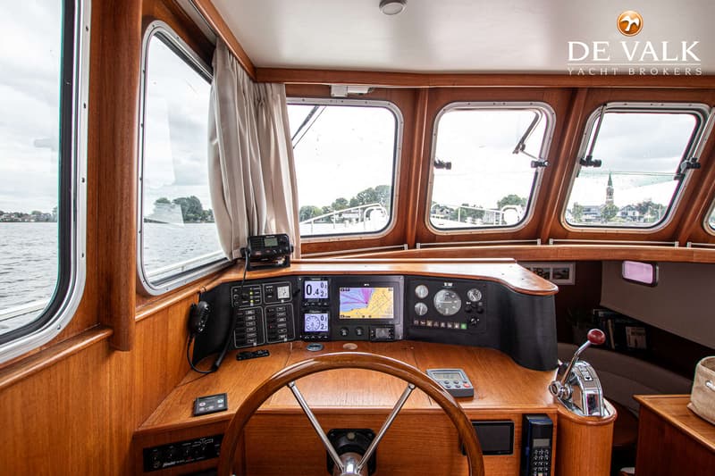Een houten stuurwiel en een dashboard met navigatieschermen en meters zijn zichtbaar in de kajuit van een boot.
