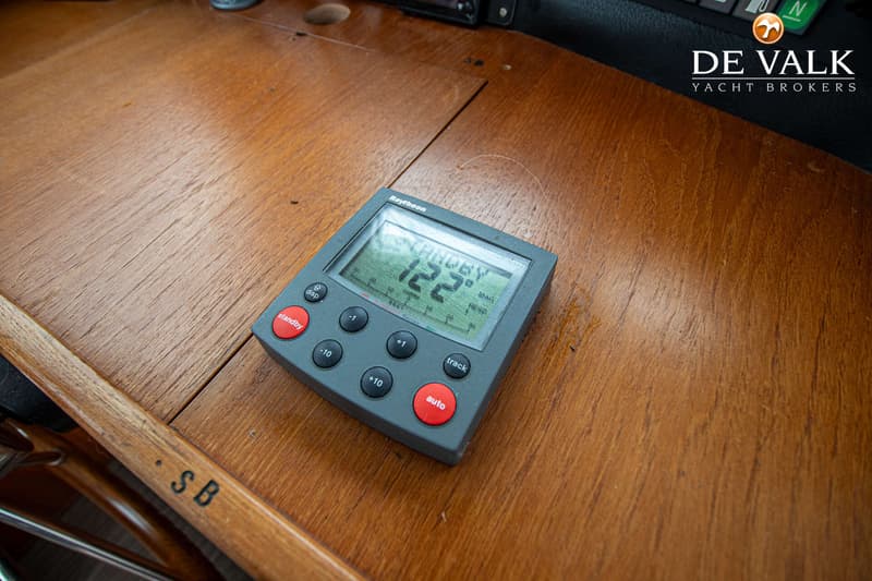 Een Raytheon-apparaat met een digitaal display dat "STANDBY 122" toont, ligt op een houten oppervlak.