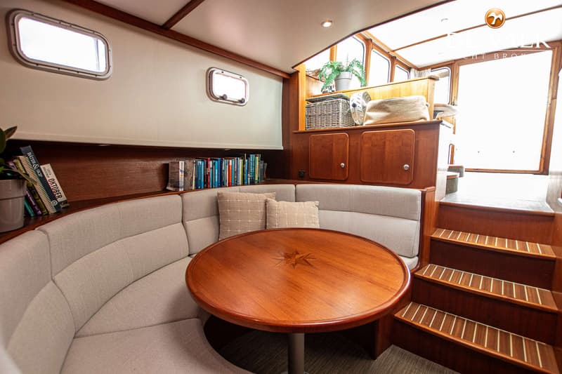 De foto toont het interieur van een boot met een ronde houten tafel, een U-vormige bank en een trap. — Combi Kotter 1300