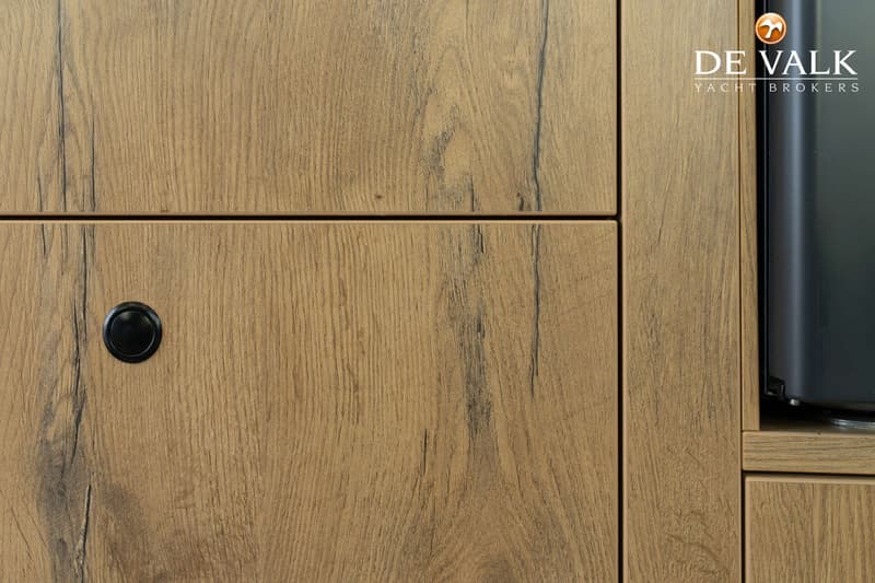 Een detail van een houten kast met een zwarte knop en een deel van een zwart apparaat.