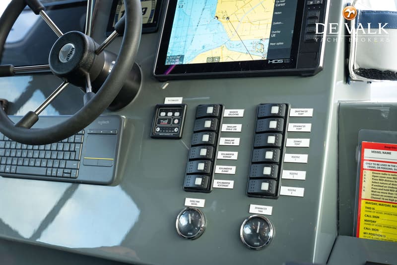 Een stuurwiel, een toetsenbord, een navigatiescherm, schakelaars en meters zijn zichtbaar op het dashboard van een boot.