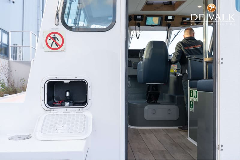 Een open luik met een joystick en een man in een stuurhut met een stuur en navigatieschermen.