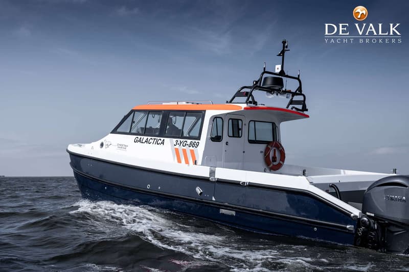 Een witte en blauwe boot met oranje accenten en de naam "GALACTICA" vaart op water onder een bewolkte lucht.