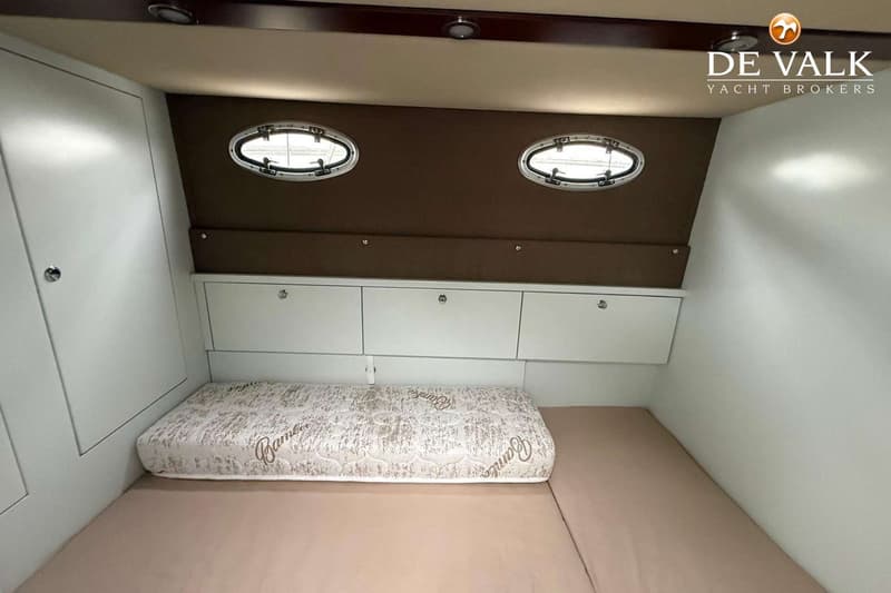 Een kajuit met een bed, drie kasten, twee patrijspoorten en een "De Valk Yacht Brokers" logo. — Lobster 42 OC