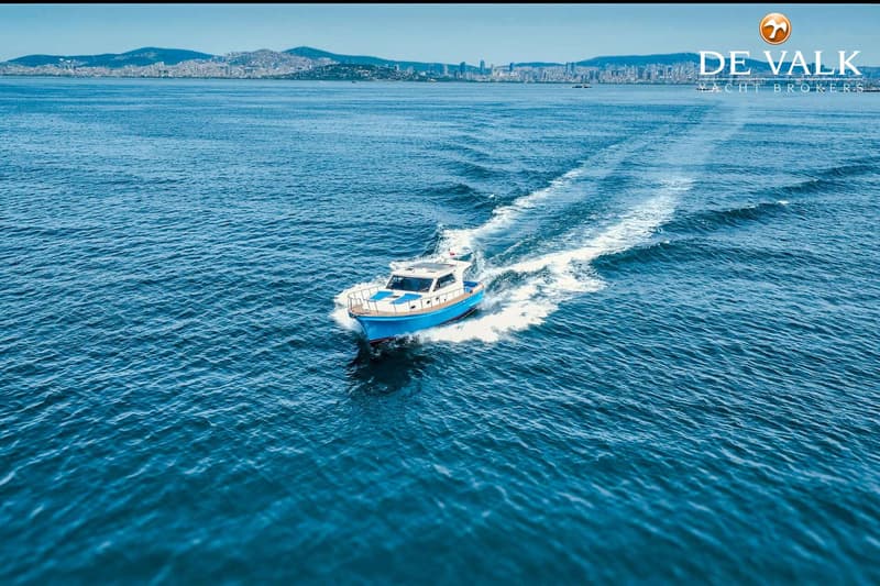Een blauw-witte motorboot vaart over een kalme zee, met een stad en bergen op de achtergrond. — Lobster 42 OC