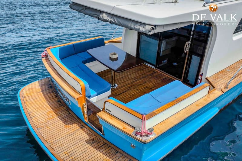 Een blauwe boot met een houten dek en blauwe kussens op de banken, met een tafel in het midden. — Lobster 42 OC