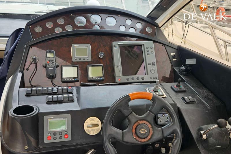 De foto toont een stuurstand met diverse meters, displays, schakelaars en een stuurwiel.