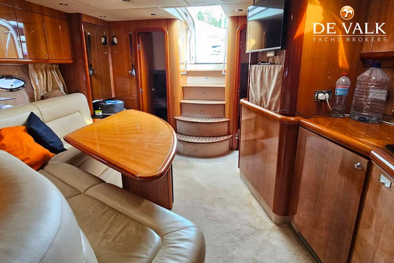 De foto toont het interieur van een boot met een zithoek, een tafel, een trap en houten kasten. — Sunseeker Portofino 53