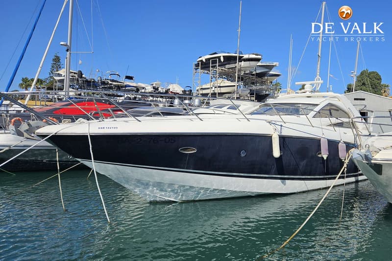 Een witte en donkerblauwe motorboot ligt afgemeerd in een haven, met andere boten op de achtergrond. — Sunseeker Portofino 53