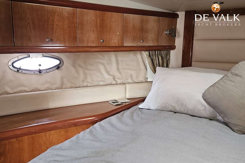 Een kajuit met een bed, een patrijspoort, houten kasten en een logo van "DE VALK YACHT BROKERS". — Sunseeker Portofino 53