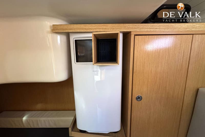 Een witte Equation airconditioner staat naast een houten kast met een zilveren slot.
