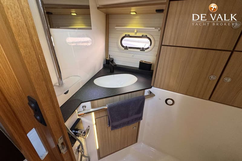 Een badkamer met een wastafel, een spiegel, een patrijspoort en houten kasten.