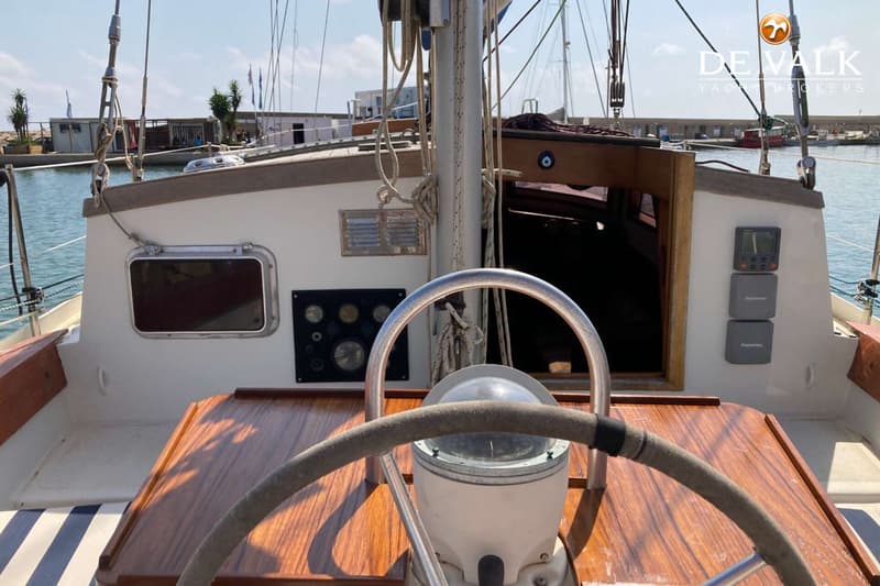 Een stuurwiel met kompas en een houten dashboard met diverse meters zijn zichtbaar in de kuip van een zeilboot.