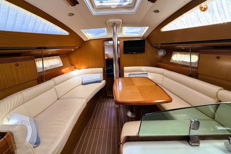 De foto toont het interieur van een boot met een houten vloer, crème banken, een houten tafel en een televisie.