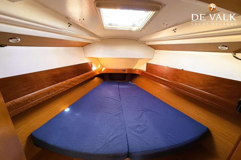 De foto toont een kajuit met een V-vormig bed met blauwe matrassen, houten zijpanelen en een dakluik.