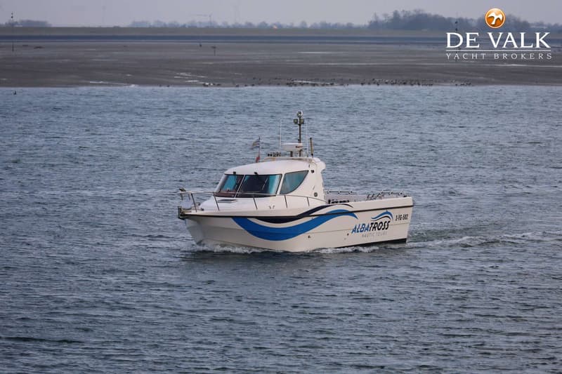 Een witte boot met blauwe accenten en de tekst "ALBATROSS NAUTIC TOURS" vaart op water met een zandbank op de achtergrond.