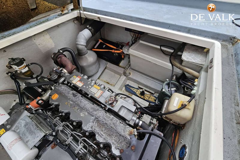 De foto toont een motorruimte met een grijze scheepsmotor, diverse slangen, filters en een accu.