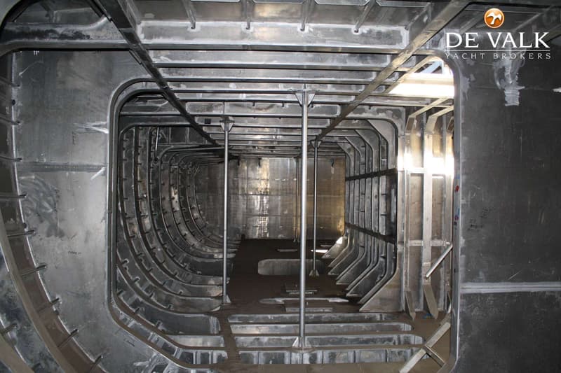 De foto toont de onafgewerkte, metalen binnenkant van een scheepsromp met spanten, liggers en steunpilaren.