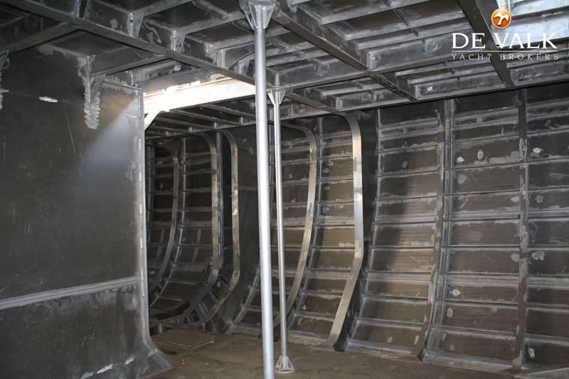 De foto toont het onafgewerkte, metalen interieur van een boot met zichtbare spanten en verstevigingen.