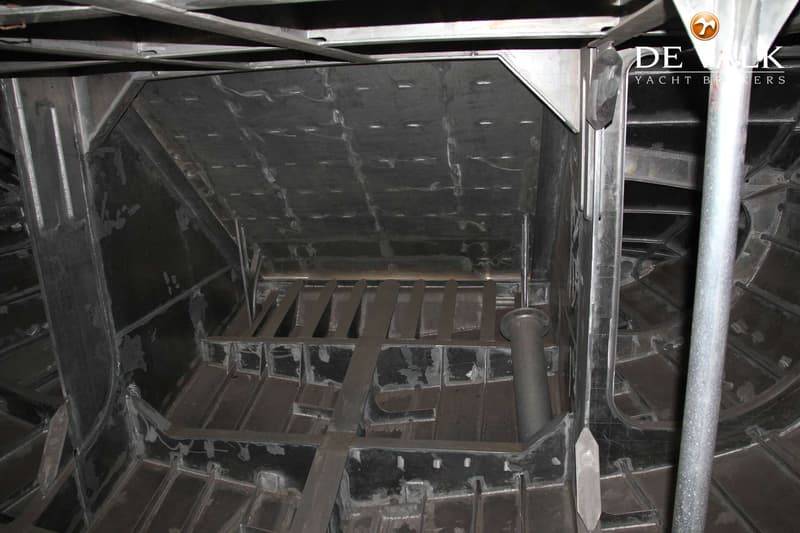 Een onafgewerkte, metalen scheepsromp met zichtbare spanten en verstevigingen.