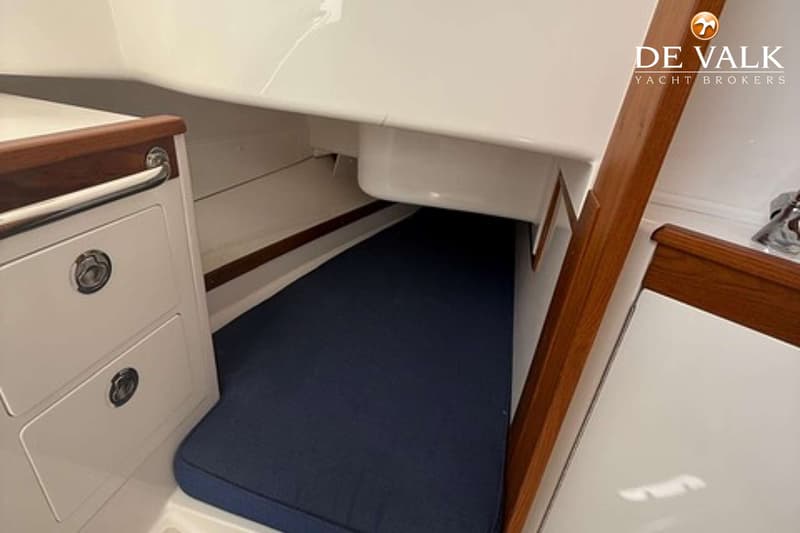 Een kajuit met een donkerblauw matras, witte wanden, houten accenten en twee lades met zilveren handgrepen.