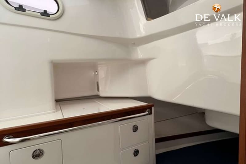 Een witte kajuit met een patrijspoort, een houten rand, lades en een handgreep. — Hunt Surfhunter 33