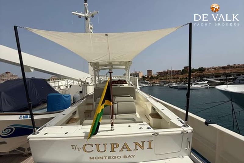 Een witte boot met de naam "T/T CUPANI MONTEGO BAY" op de spiegel, met een Jamaicaanse vlag en een zonnescherm.