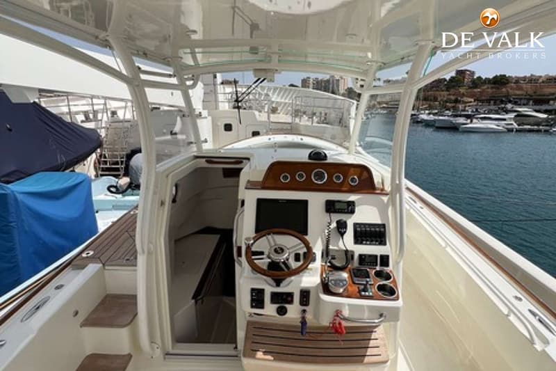 De foto toont de stuurstand van een boot met een houten stuurwiel, diverse meters en schakelaars, en een scherm.