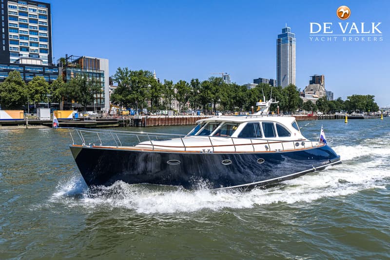 Een donkerblauwe motorboot met een witte opbouw vaart over water, met een stad op de achtergrond. — Rapsody 55