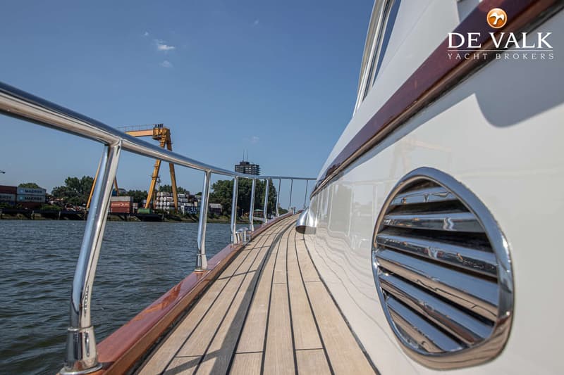Een zijaanzicht van een boot met een houten dek, een metalen reling en een ronde ventilatieopening. — Rapsody 55