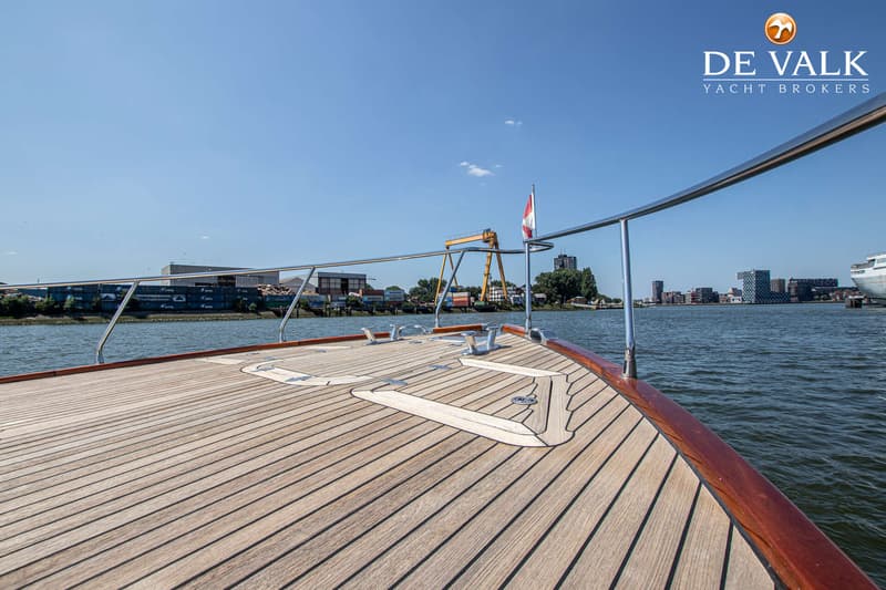 Een teakdek met een roodbruine houten rand en een roestvrijstalen reling, met een Nederlandse vlag aan stuurboord.