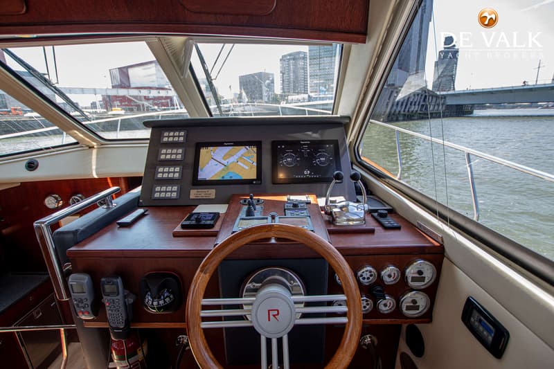 De foto toont het stuurhuis van een boot met een houten stuurwiel, navigatieschermen en diverse bedieningselementen.