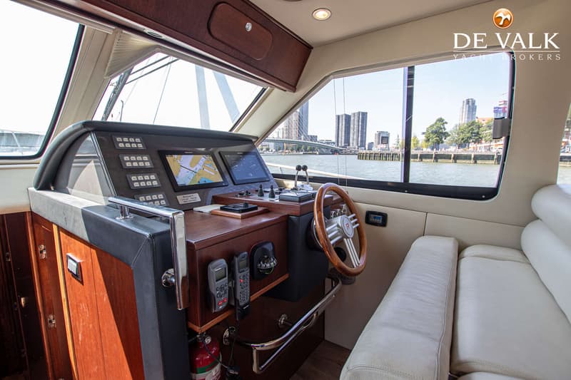 De foto toont het interieur van een boot met een stuurwiel, navigatieschermen en een uitzicht op een stad aan het water.
