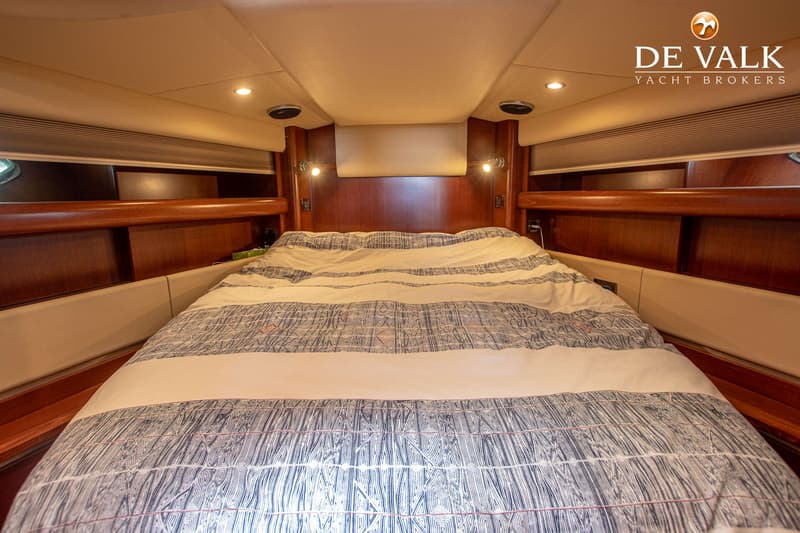 Een kajuit met een tweepersoonsbed met een wit-blauw gestreept dekbed, omringd door houten panelen en beige bekleding.
