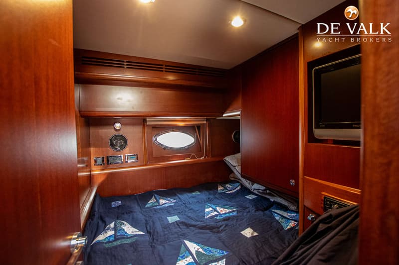 De foto toont een kajuit met een bed met een donkerblauw dekbed met zeilbootmotieven, houten wanden en een patrijspoort.