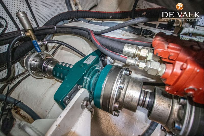 Een detailfoto van een scheepsmotor met diverse leidingen, koppelingen en een groen onderdeel.