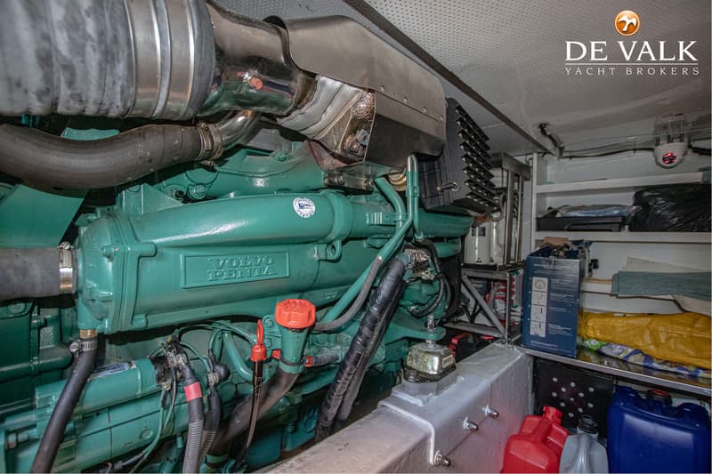 Een detailfoto van een groene Volvo Penta scheepsmotor met slangen, kabels en een rode dop, in een motorruimte met opslag.