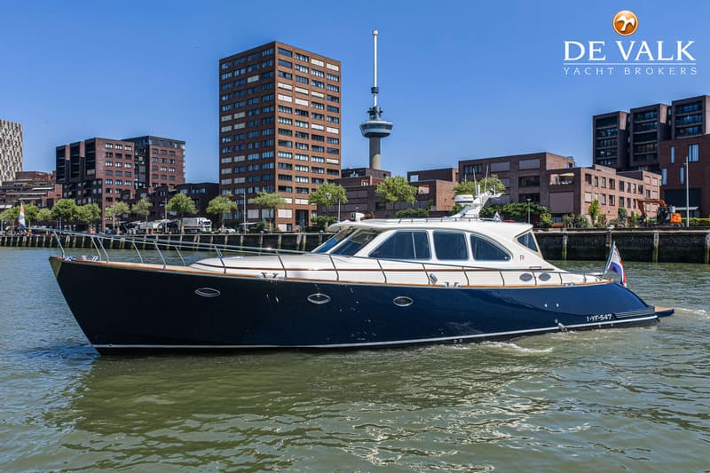 Een blauw-witte motorboot vaart op het water met gebouwen en een toren op de achtergrond. — Rapsody 55