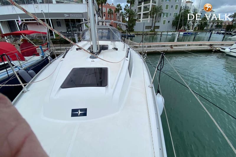 Een witte zeilboot ligt aangemeerd in een haven, met een man in de kuip en gebouwen op de achtergrond. — Bavaria 34 Cruiser