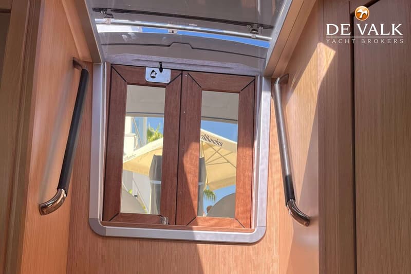 Een houten interieur met een raam met houten kozijnen en een metalen handgreep aan weerszijden.