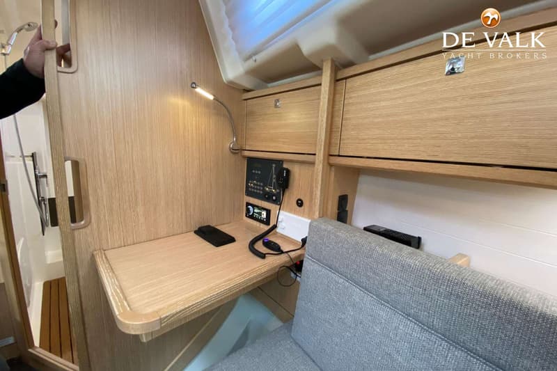 Een interieur van een boot met een houten bureau, een grijze bank, een douchecabine en diverse elektronische apparatuur.