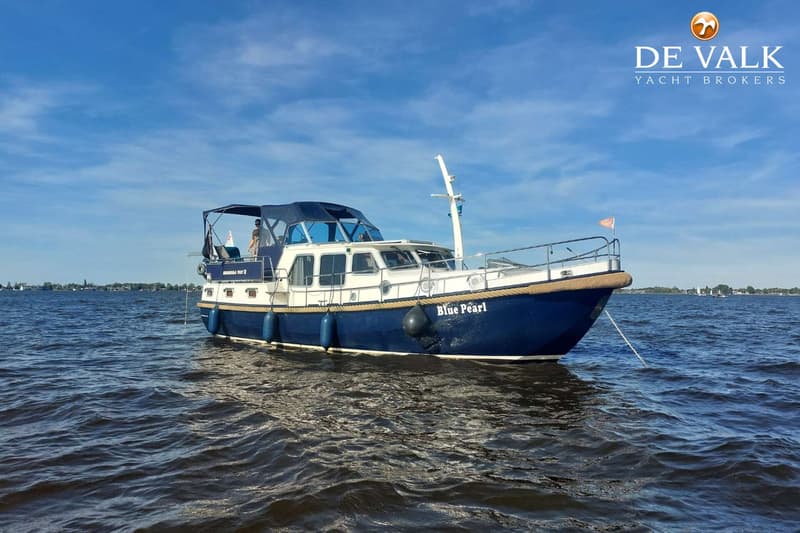 Een blauw-witte motorboot met de naam "Blue Pearl" ligt op het water onder een blauwe lucht met wolken.