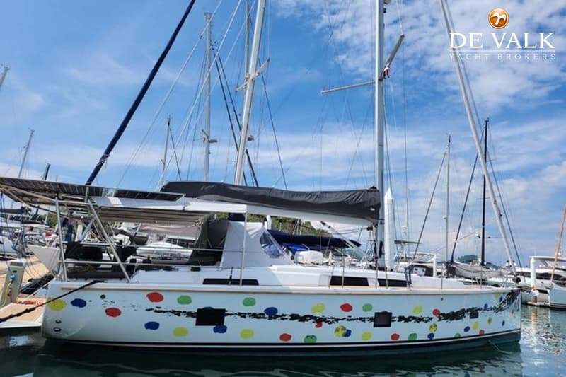 Een witte zeilboot met kleurrijke stippen en zwarte strepen op de romp ligt in een haven onder een blauwe lucht. — Hanse 458
