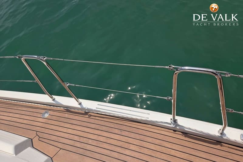 Een dek van een boot met houten planken en een metalen reling, met groen water op de achtergrond. — Hanse 458