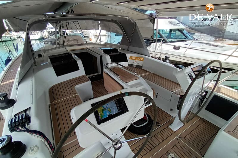 Een witte zeilboot met teakhouten dek en twee stuurwielen, waarvan één met een navigatiescherm. — Hanse 458