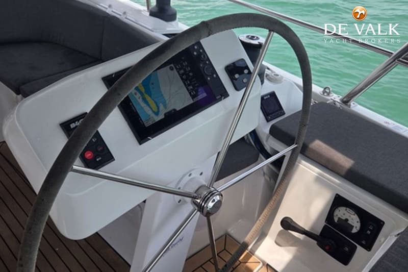 Een stuurwiel met een navigatiescherm en diverse bedieningspanelen, met de zee op de achtergrond.
